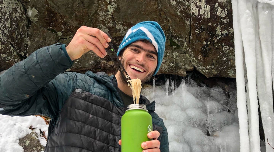 Winter outdoor sport nutrition Man with a frozen beard smiling Man ice climbing with rope and picks. smiling man eating left over noodle dinner from thermos.